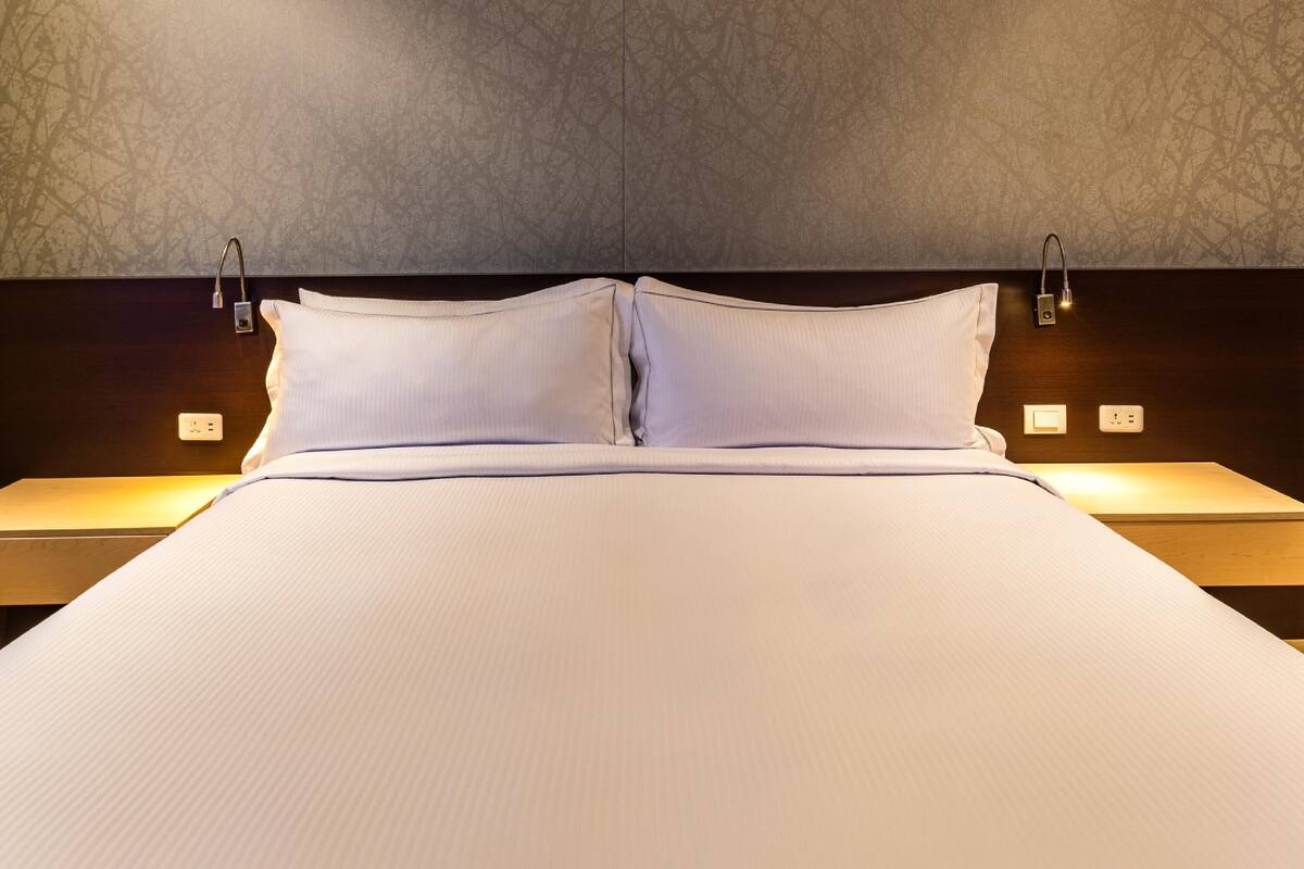A neatly made bed with white linens, a dark headboard, and two bedside lamps.