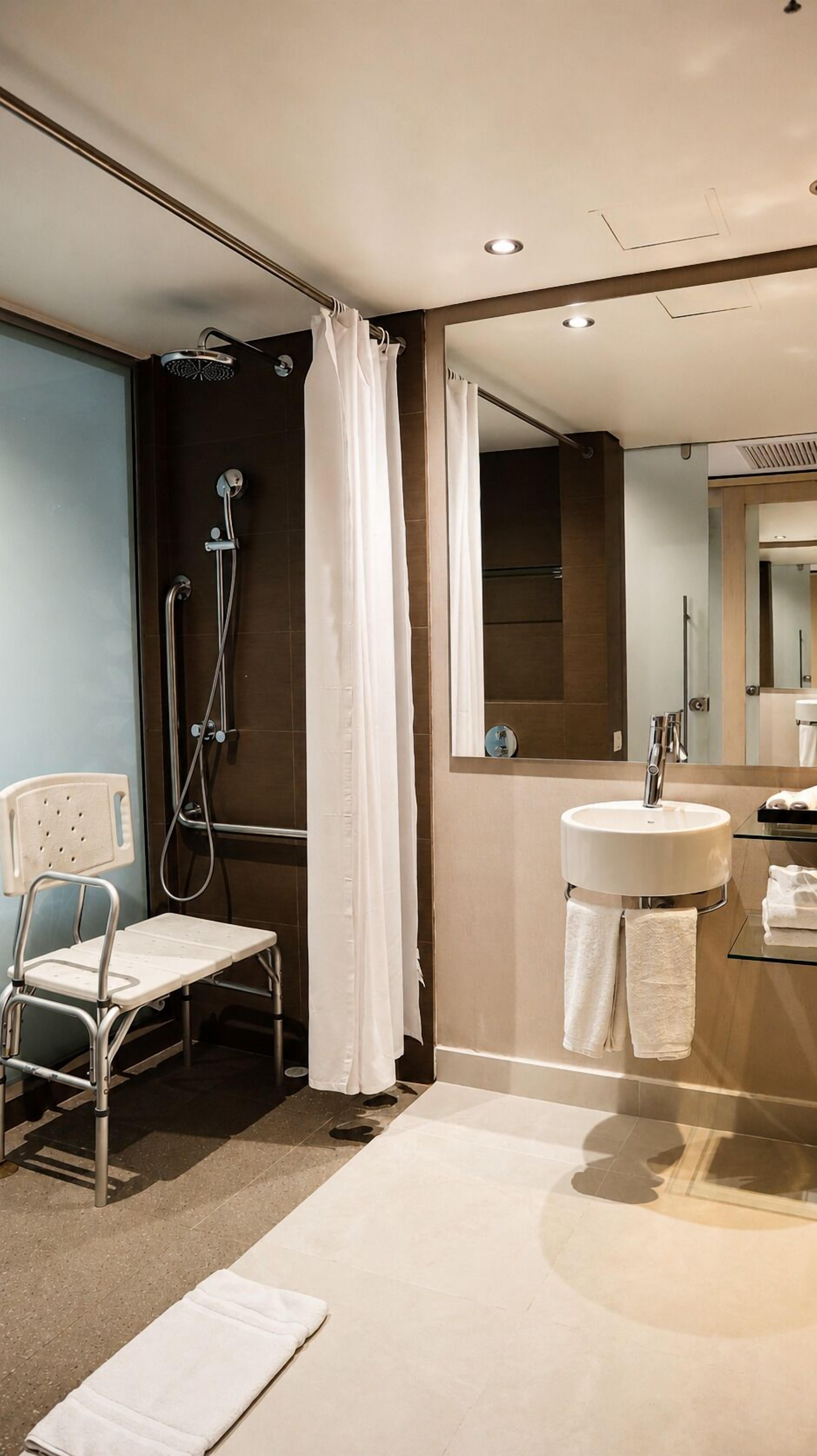 A modern bathroom with a shower, a sink, a chair, and a mirror.