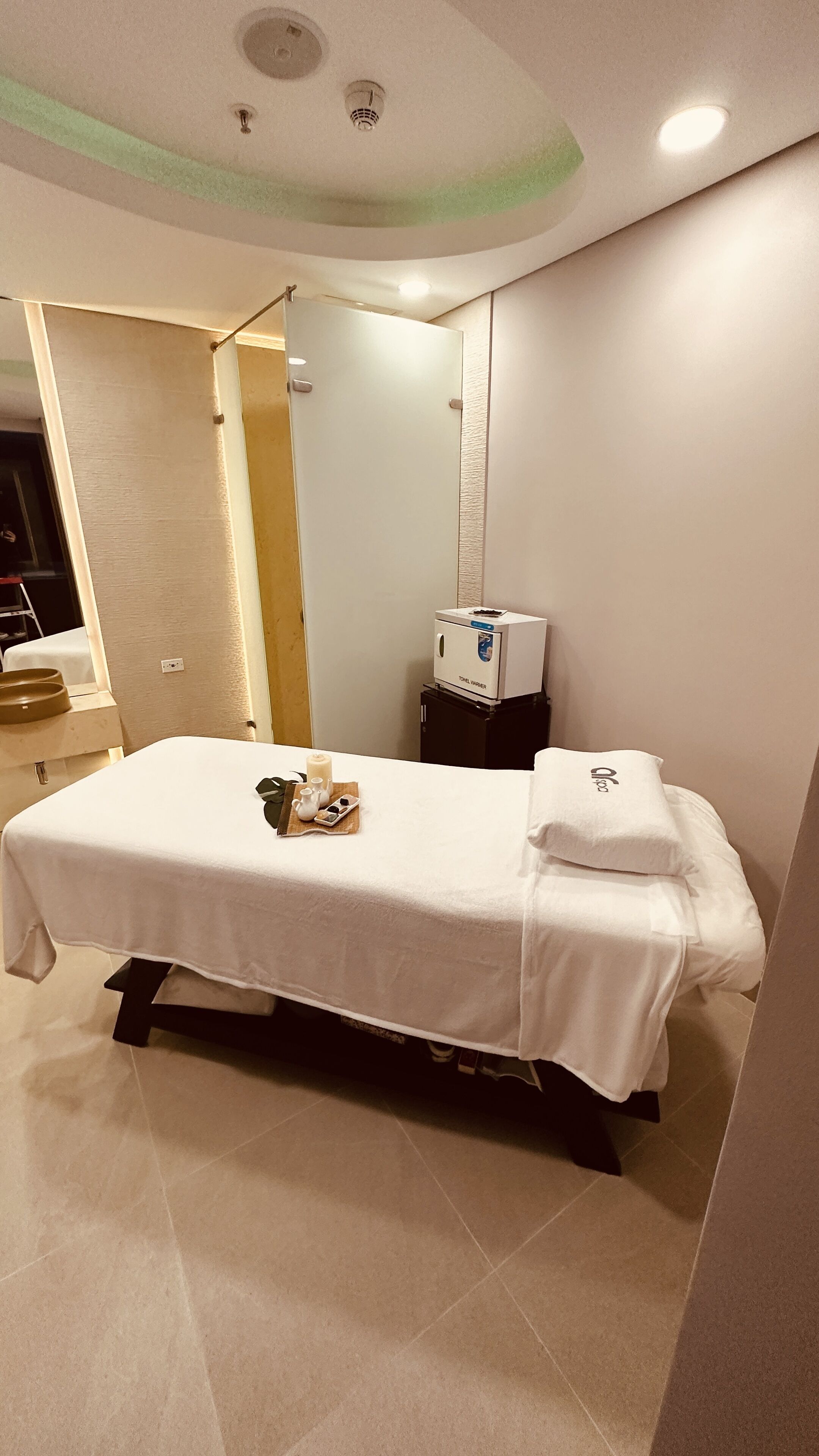 A hotel room with a bed, a towel warmer, a sink, and a mirror.