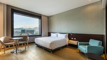 A hotel room with a large window, a bed, two chairs, a small table, and a nightstand.