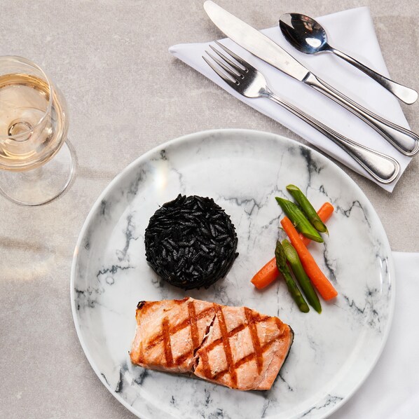 Un plato con salmón a la parrilla, arroz negro y verduras sobre una mesa de mármol.
