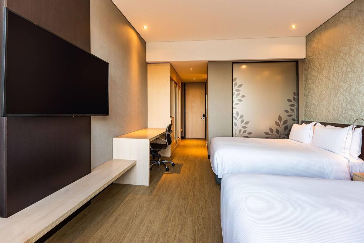 A hotel room with a TV, a desk, two beds, and a door leading to a hallway.