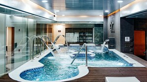 Un área de piscina interior moderna con varios jacuzzis, paredes de vidrio y suelo de madera.