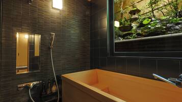 Un baño moderno con una bañera de madera, un espejo y vistas a un jardín a través de una ventana.