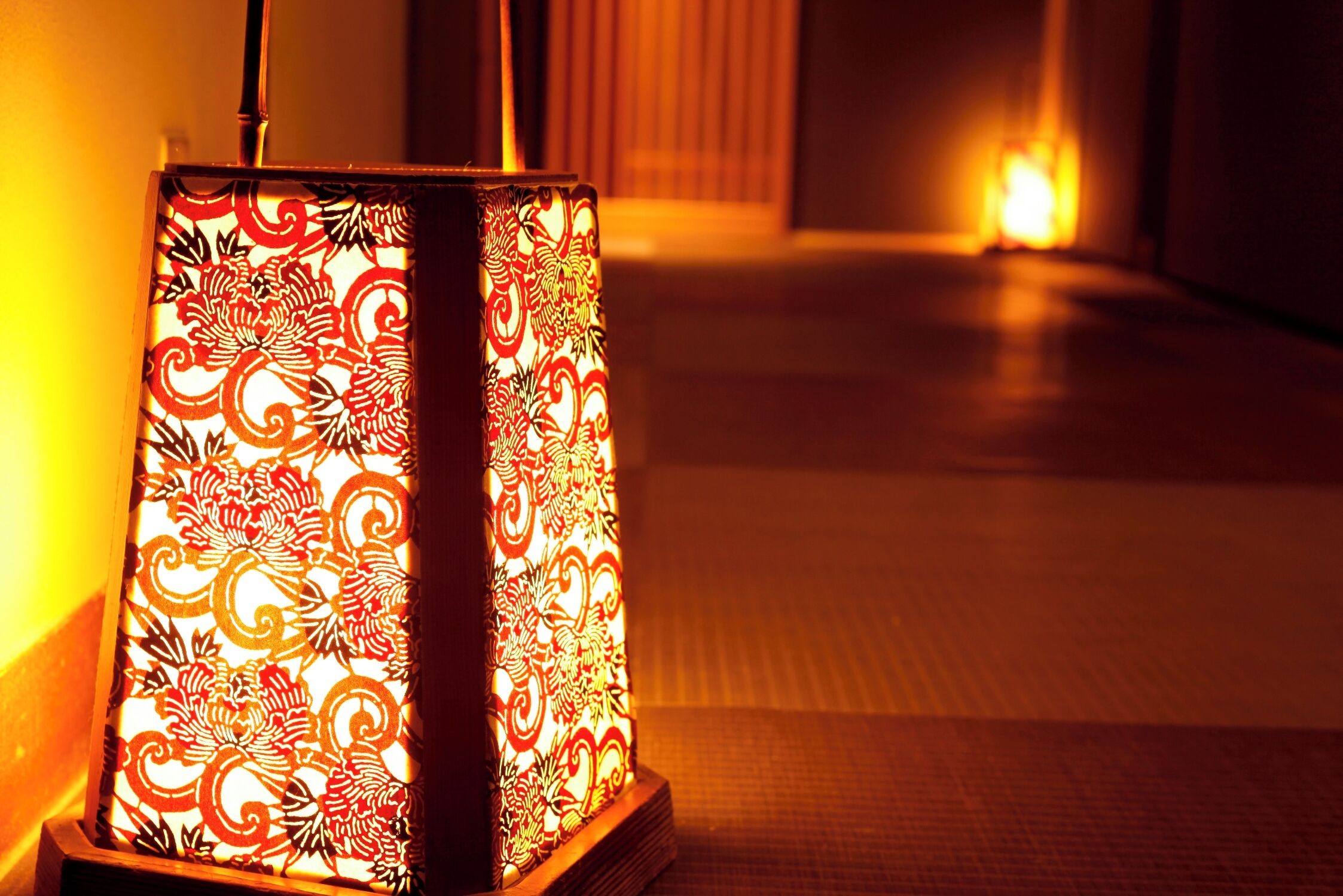 A traditional Japanese paper lantern with intricate patterns, placed on a wooden stand in a hallway.