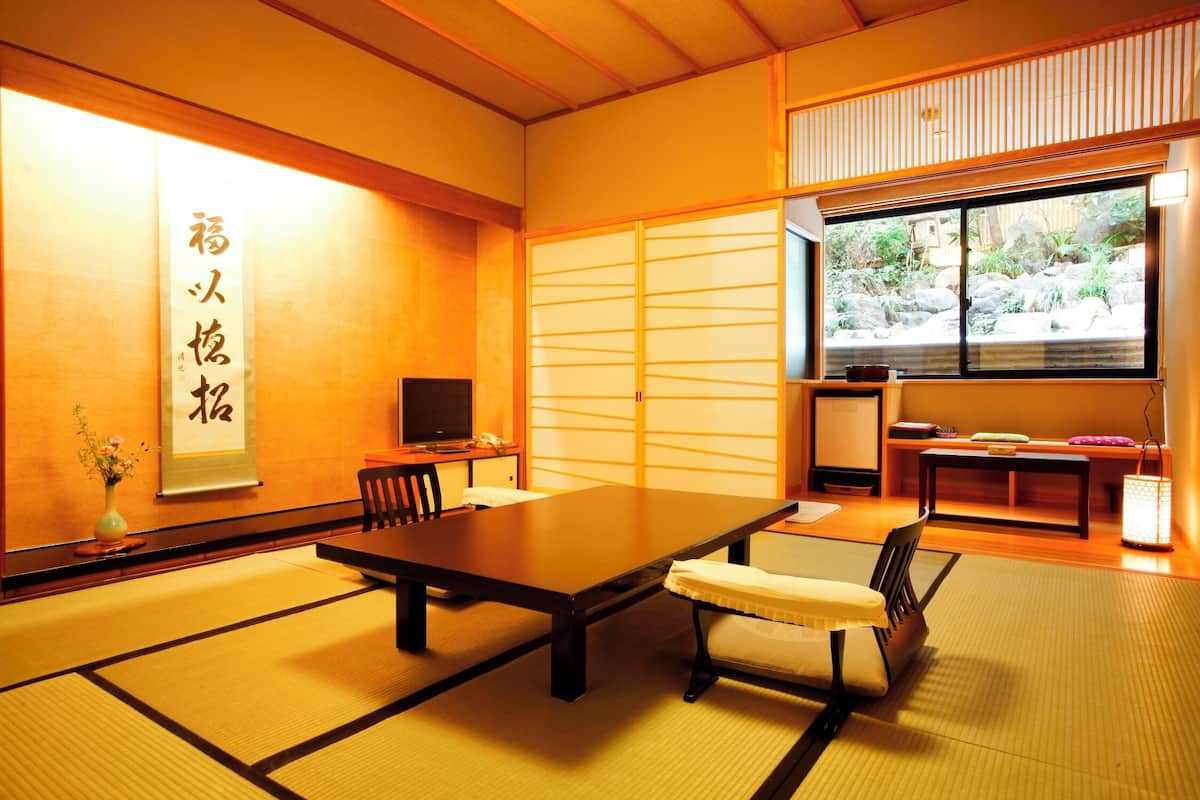 Ett traditionellt japanskt rum med tatamimattor på golvet, ett lågt bord, stolar, en TV och en skjutdörr som leder ut till en trädgård.