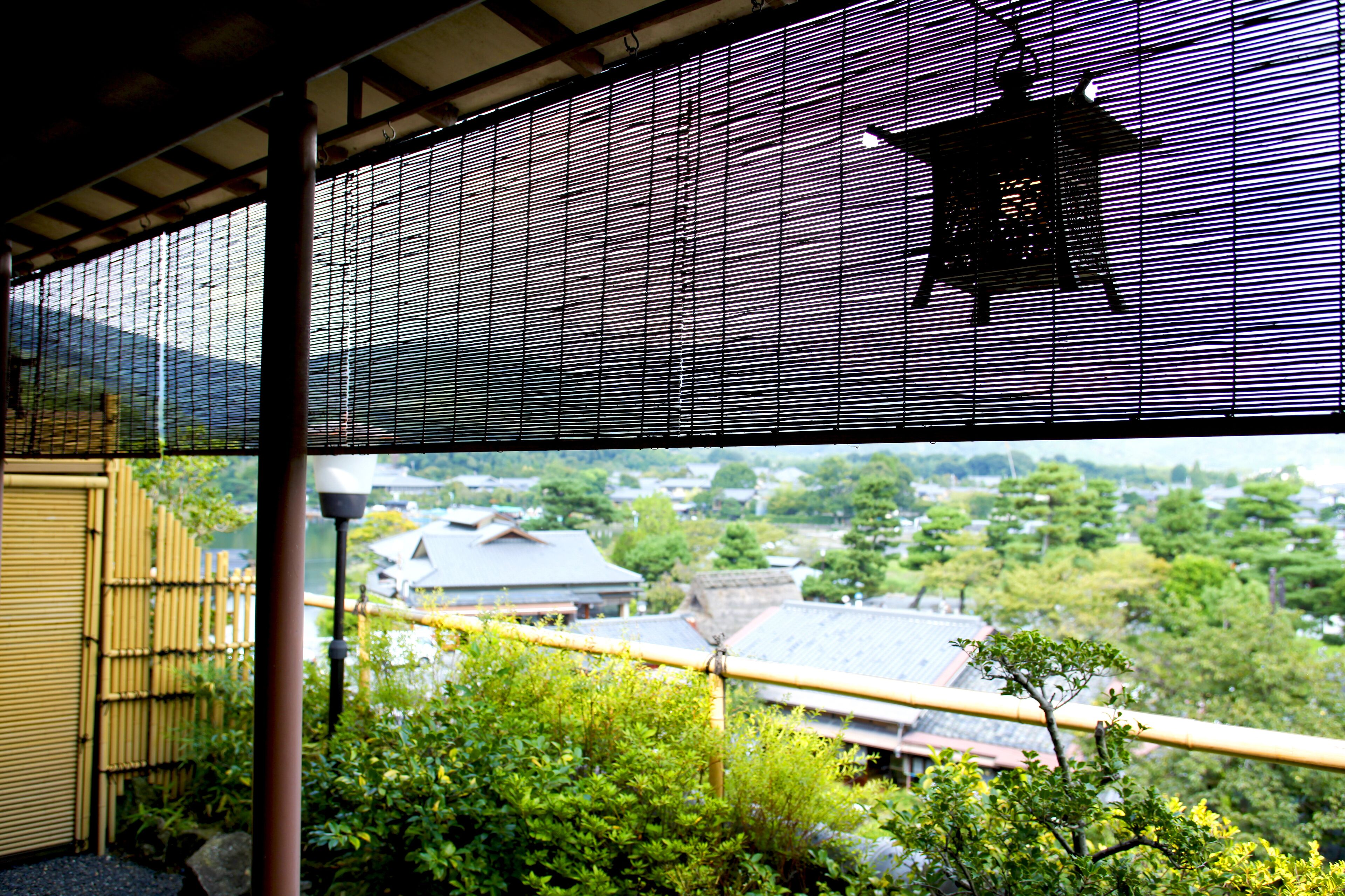 Een traditionele Japanse kamer met tatami vloerbedekking, een shoji-scherm en uitzicht op een bamboomschutting en groen buiten.