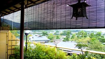 Een traditionele Japanse kamer met tatami vloerbedekking, een shoji-scherm en uitzicht op een bamboomschutting en groen buiten.