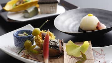 A variety of dishes on a dining table, including sushi, a dumpling, and a bowl of salad.