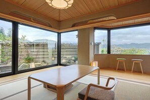 A room with a wooden table, two stools, tatami mats, and large windows offering a view of mountains. - Togetsutei (Kyoto)