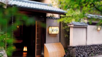 A traditional Japanese building with a wooden entrance, a stone wall, and a bamboo structure outside.
