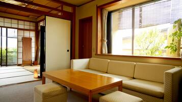 Ein traditioneller japanischer Raum mit Tatami-Böden, einem niedrigen Holztisch, einer Couch und einer Schiebetür zu einem weiteren Tatami-Raum.