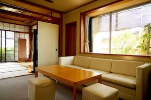 A traditional Japanese room with tatami flooring, a low wooden table, a sofa, and a sliding door leading to a tatami room.