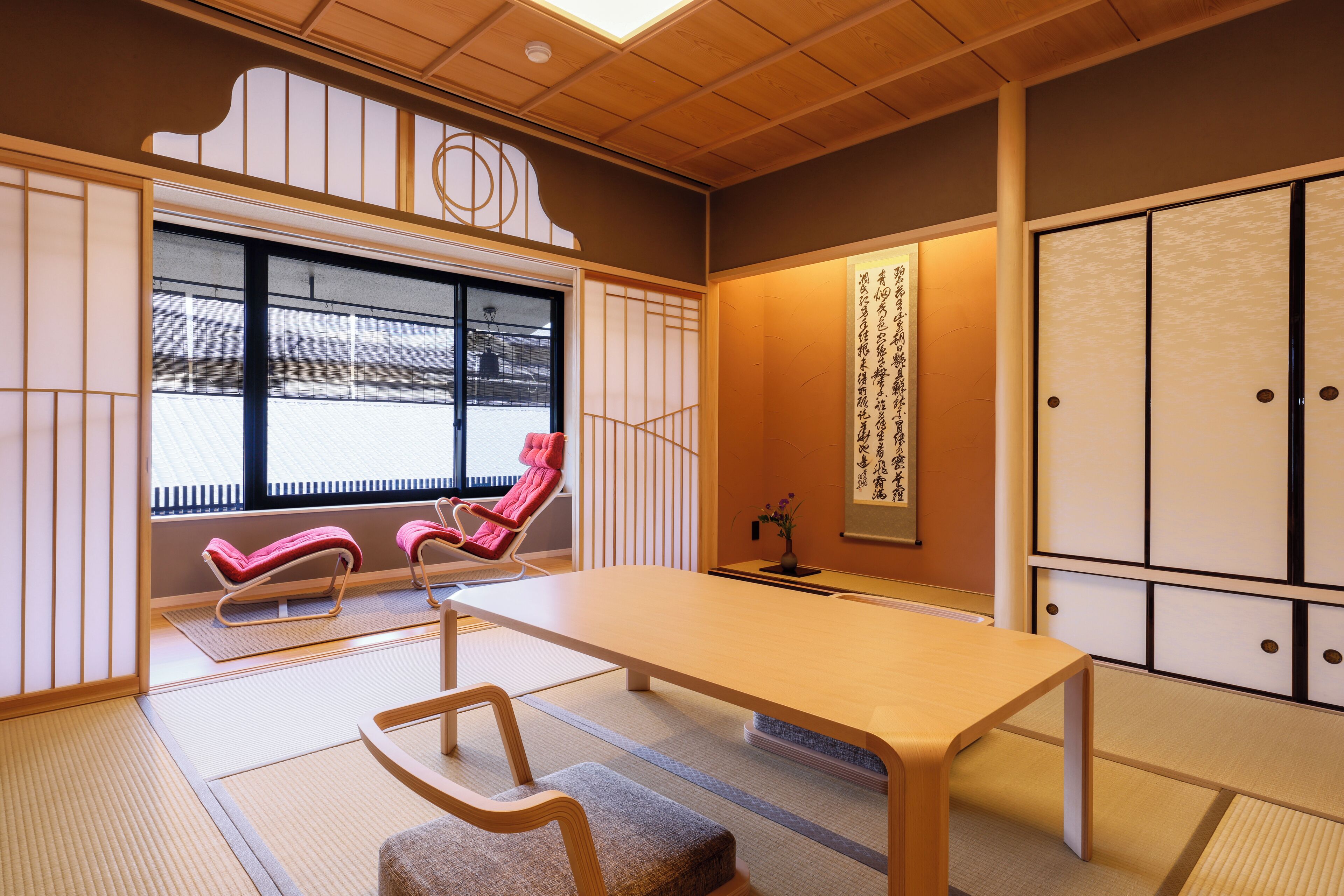 Een traditionele Japanse kamer met tatami vloerbedekking, een lage tafel, twee rode stoelen en schuifdeuren.