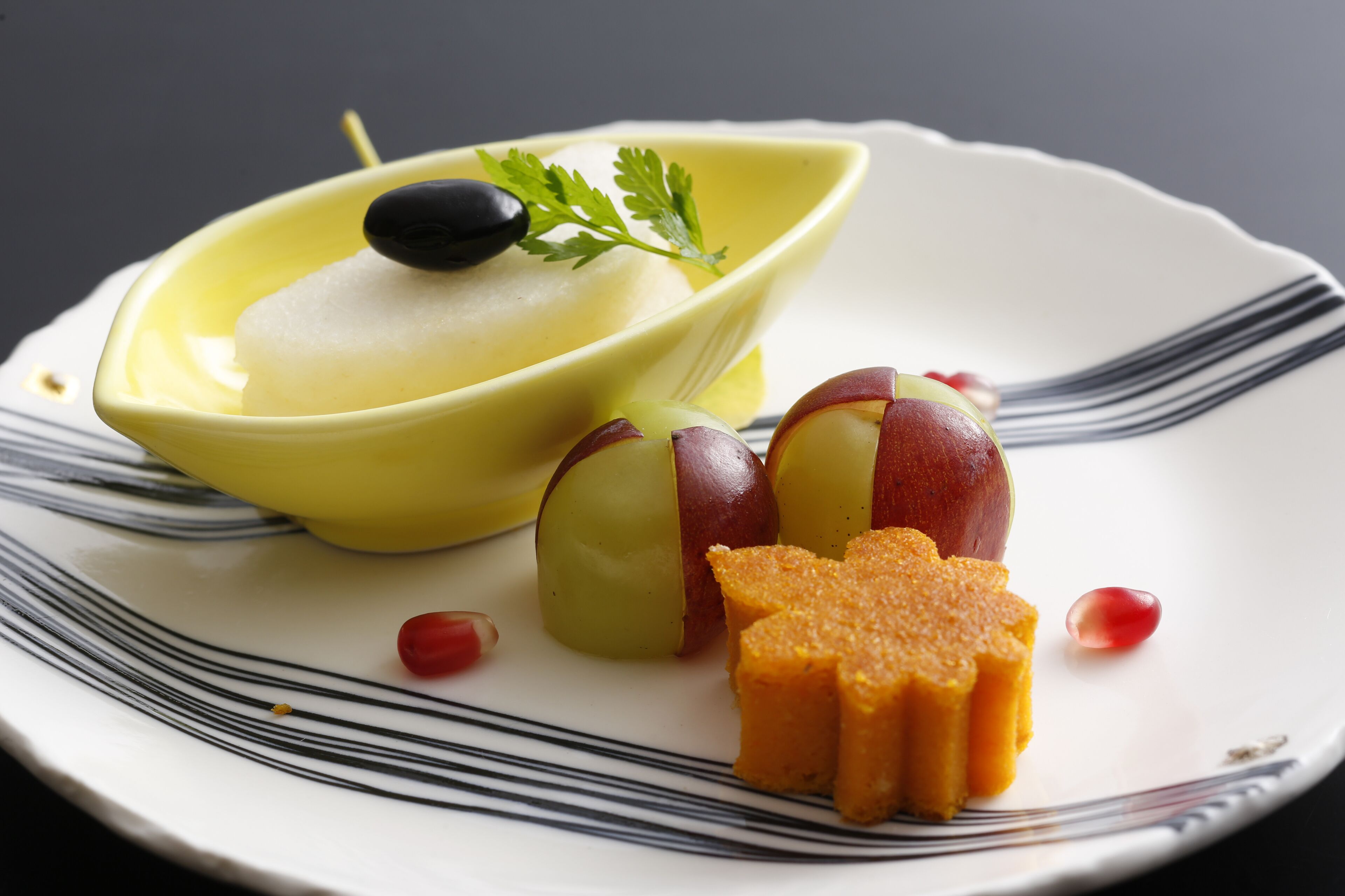 Un plato con un tazón amarillo que contiene una sustancia blanca, dos manzanas cortadas por la mitad con pulpa roja, y una porción de pastel de naranja.