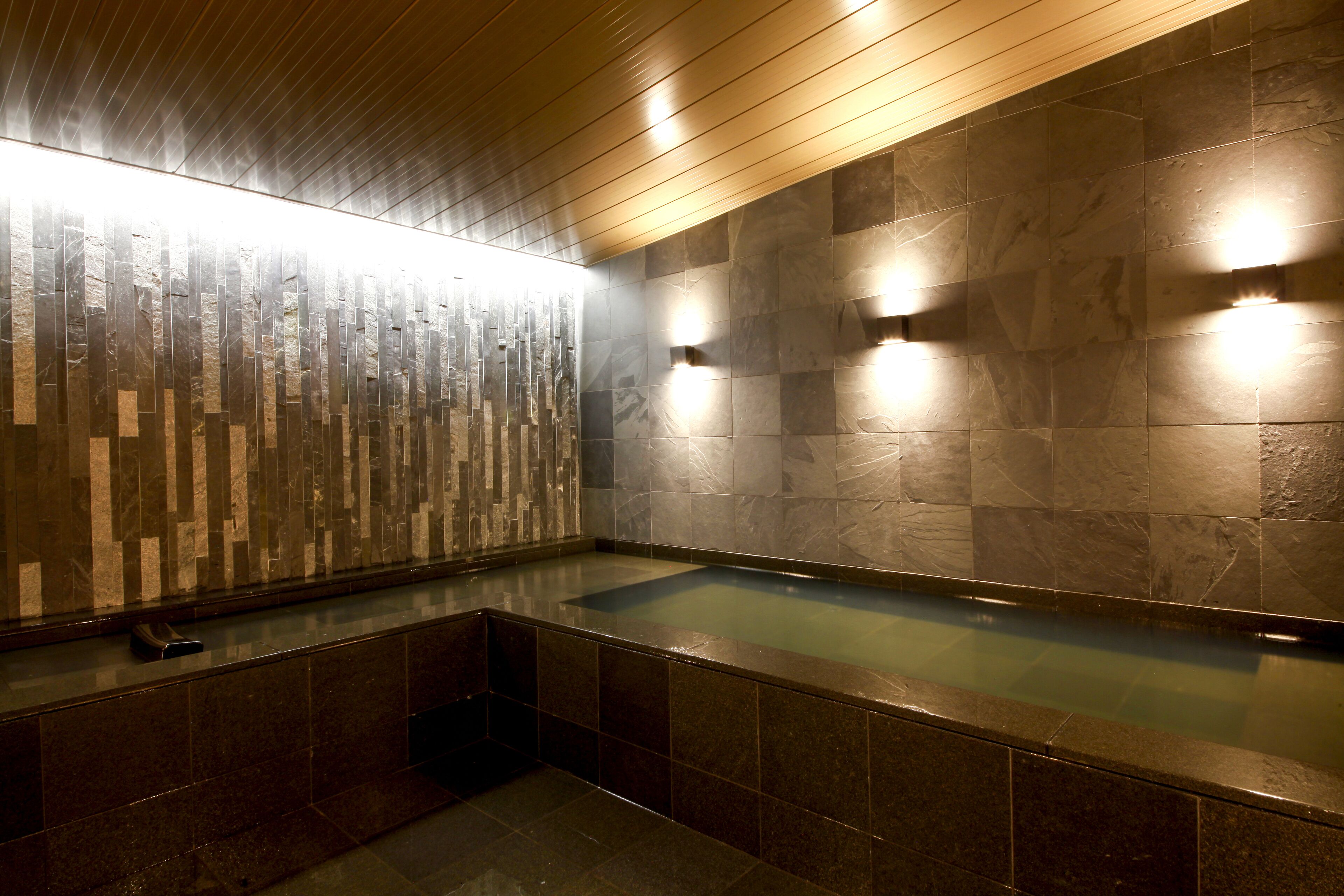 A modern bathroom with a stone wall, a wooden ceiling, and a built-in bathtub.