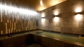 A modern bathroom with a stone wall, a wooden ceiling, and a built-in bathtub.
