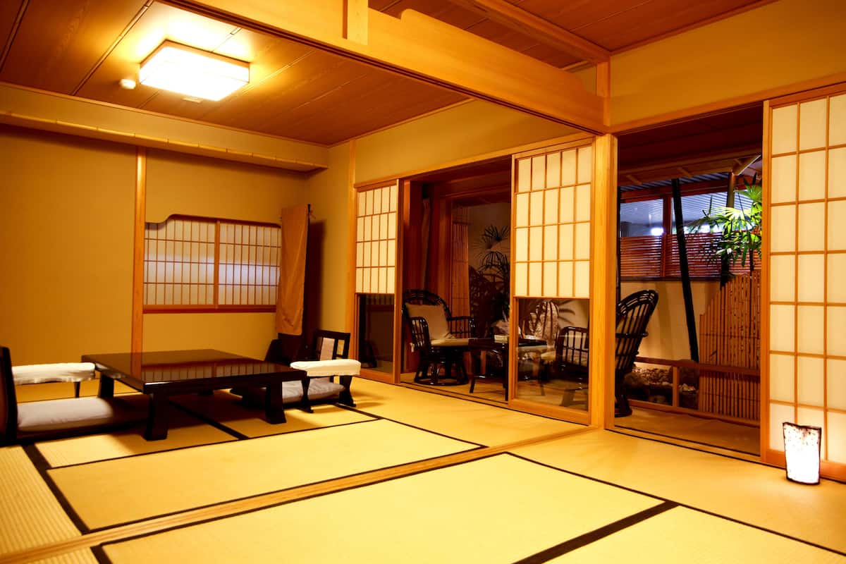Ett traditionellt japanskt rum med tatamimattor på golvet, skjutdörrar och ett lågt bord med kuddar.