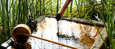 A water feature with a bamboo spout and a wooden cup, surrounded by tall green grass.