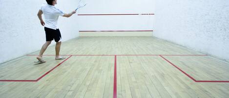 A squash court with a wooden floor and red lines marking the playing area.