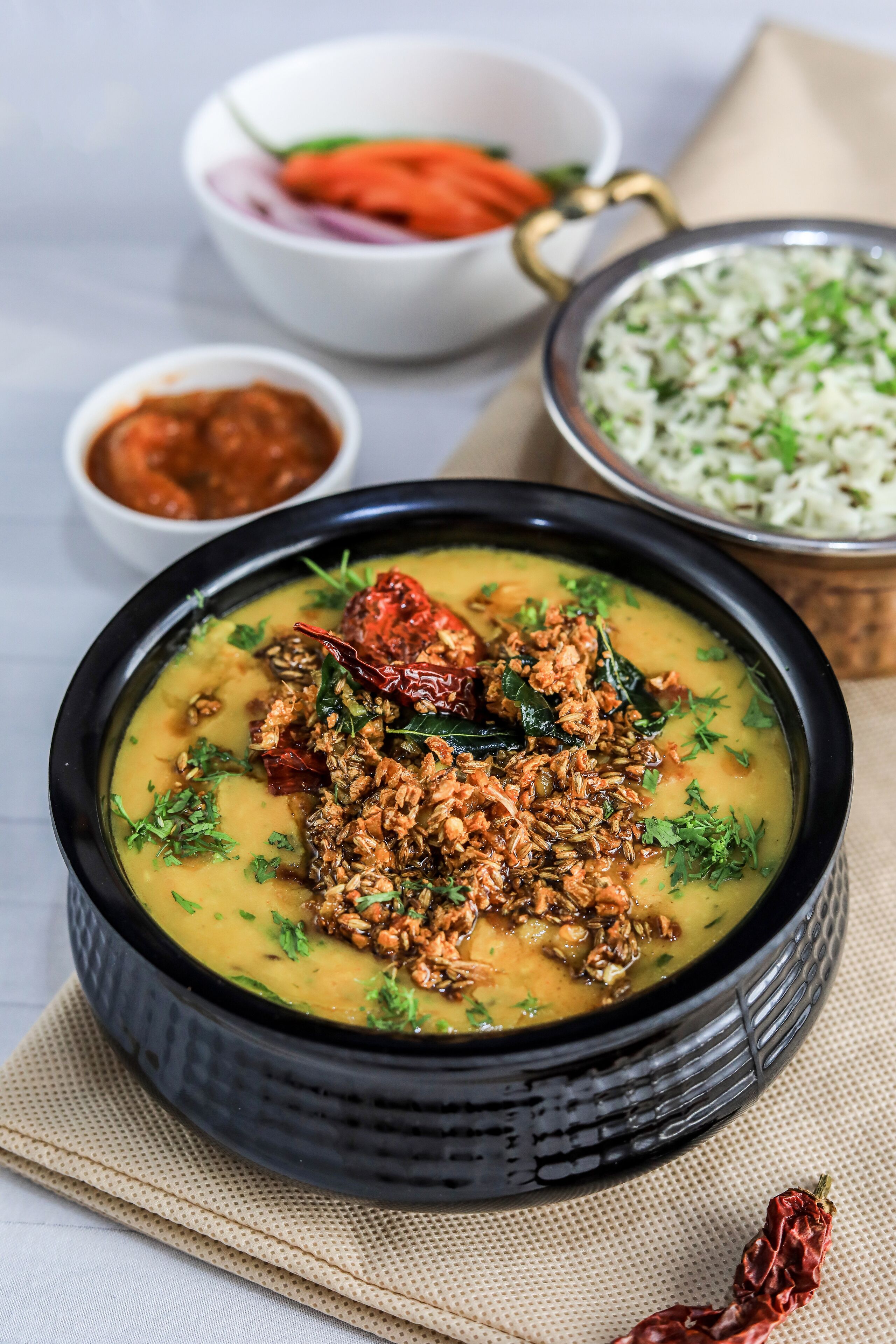 Un tazón de dal con especias y hierbas, acompañado de un tazón de arroz y un tazón pequeño de chutney.