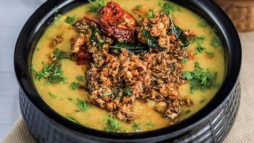 Un tazón de dal con especias y hierbas, acompañado de un tazón de arroz y un tazón pequeño de chutney.