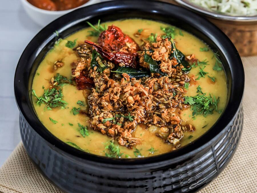 Un tazón de dal con especias y hierbas, acompañado de un tazón de arroz y un tazón pequeño de chutney.
