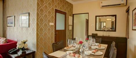 Un comedor con una mesa dispuesta para cuatro personas, sillas, un sofá rojo y un arreglo floral.