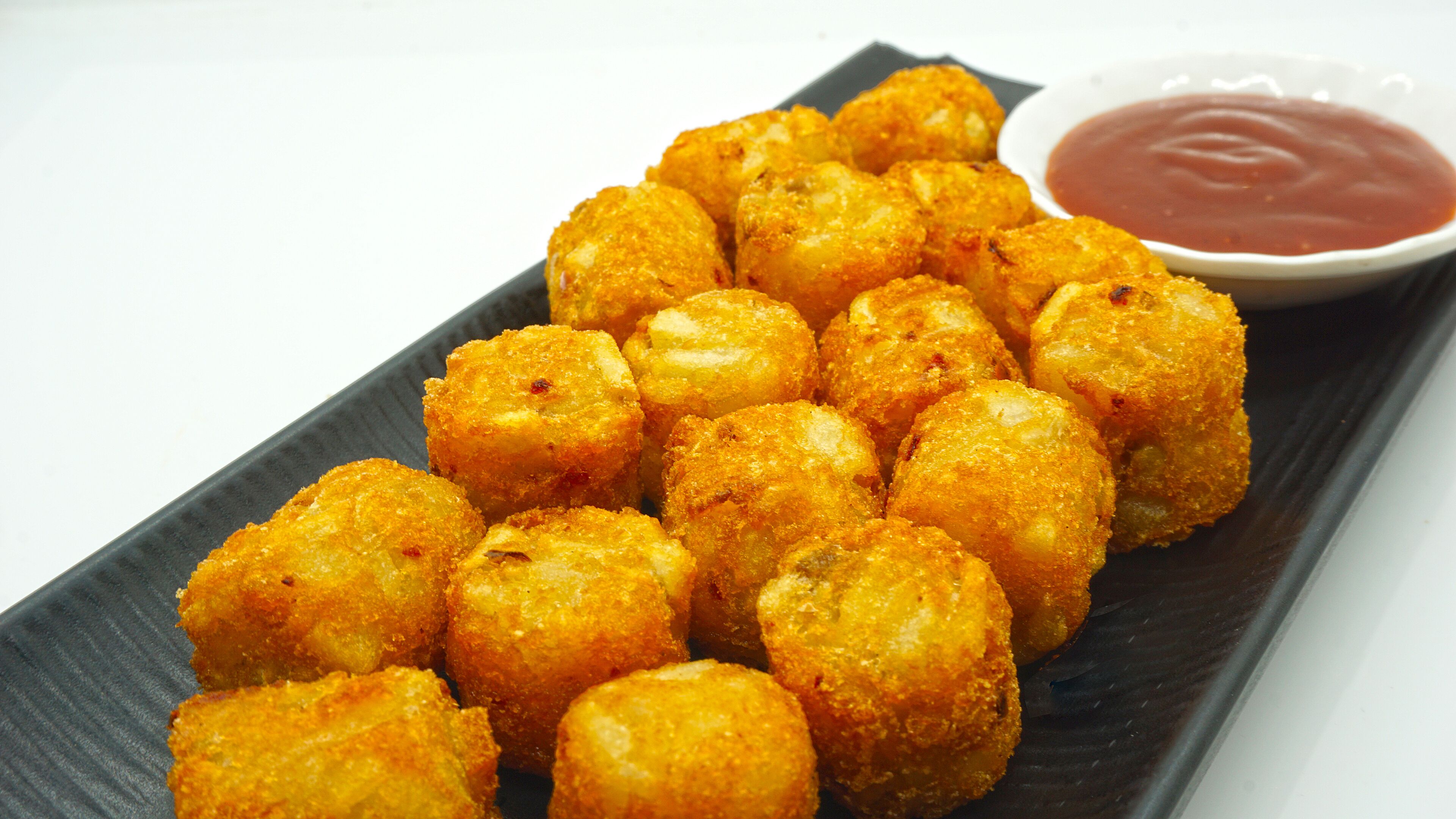 Un plato de alimentos fritos de color dorado, probablemente palitos de queso, acompañado de un pequeño recipiente con salsa roja para mojar.