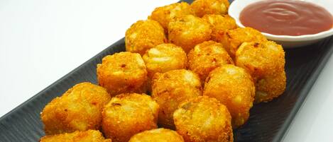 A plate of golden-brown fried food items, likely cheese sticks, accompanied by a small bowl of red dipping sauce.