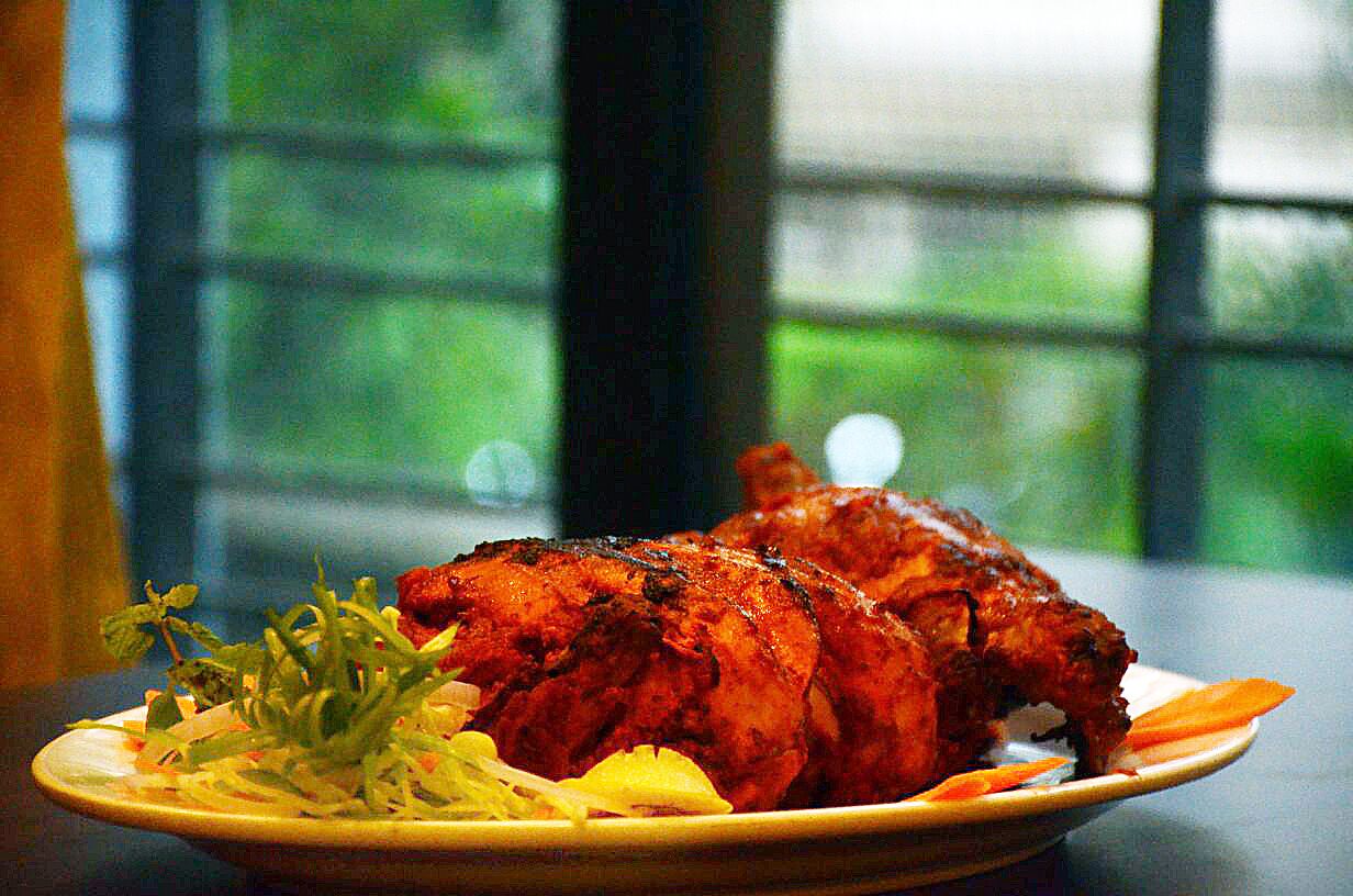 A plate of grilled chicken with vegetables on a table with a window in the background.