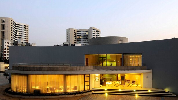 A modern hotel with a curved facade, a pool area with yellow lighting, and a visible staircase leading to the entrance. - Lalco Residency (Mumbai)