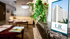 A reception area with a marble counter, a framed photo of a building, a sofa, and a table with magazines. - Lalco Residency (Mumbai)