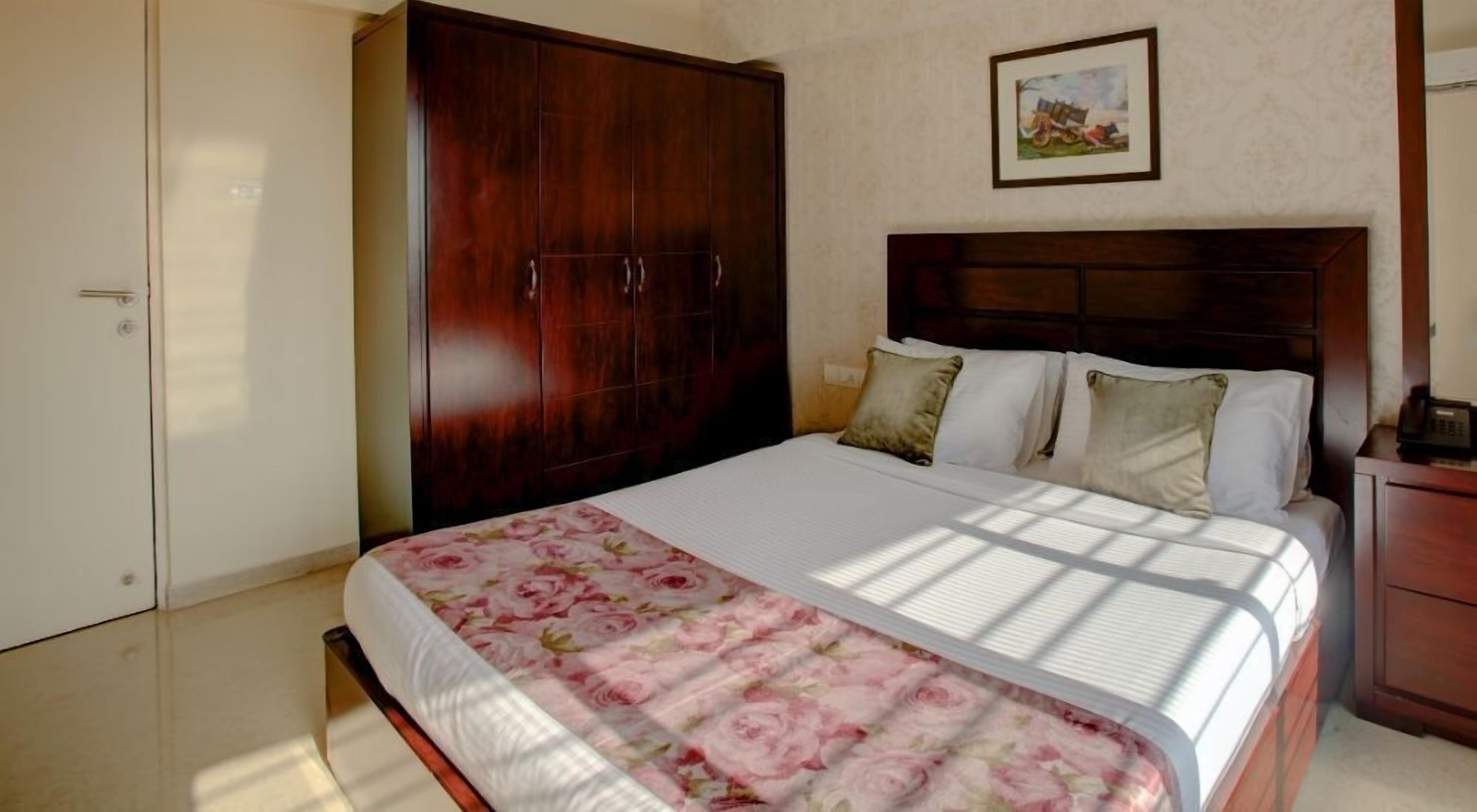 Een slaapkamer met een bed, een kledingkast, een nachtkastje en een schilderij aan de muur.