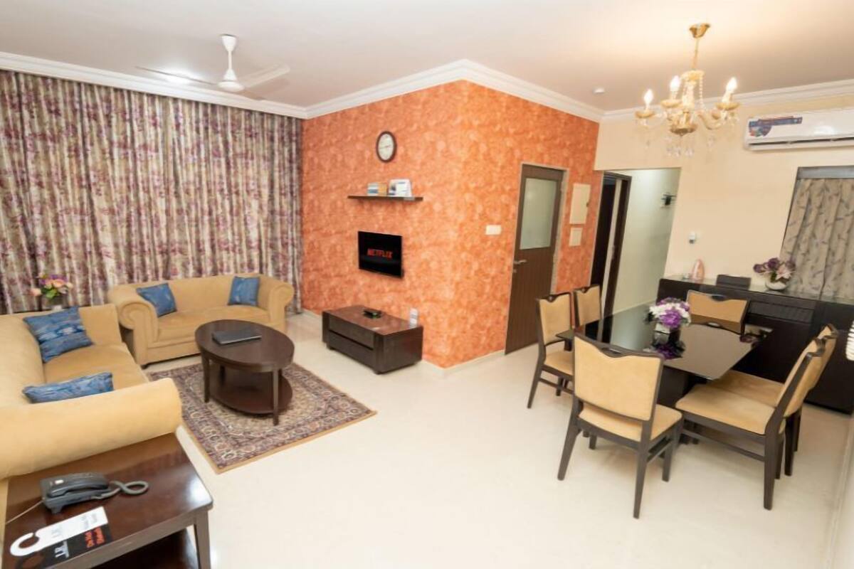 A living room with a sofa, coffee table, and TV, a dining area with chairs and a table, and a clock on the wall.