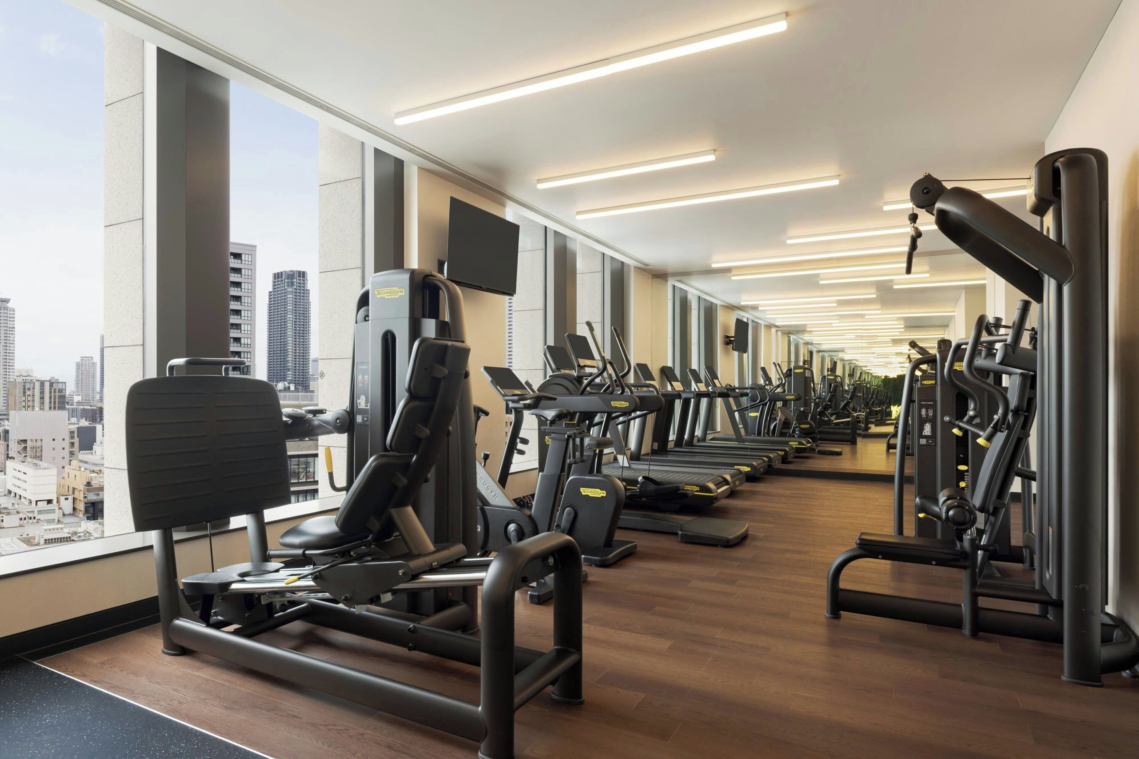 Een fitnessruimte met cardioapparatuur, krachtstations en uitzicht over de stad.