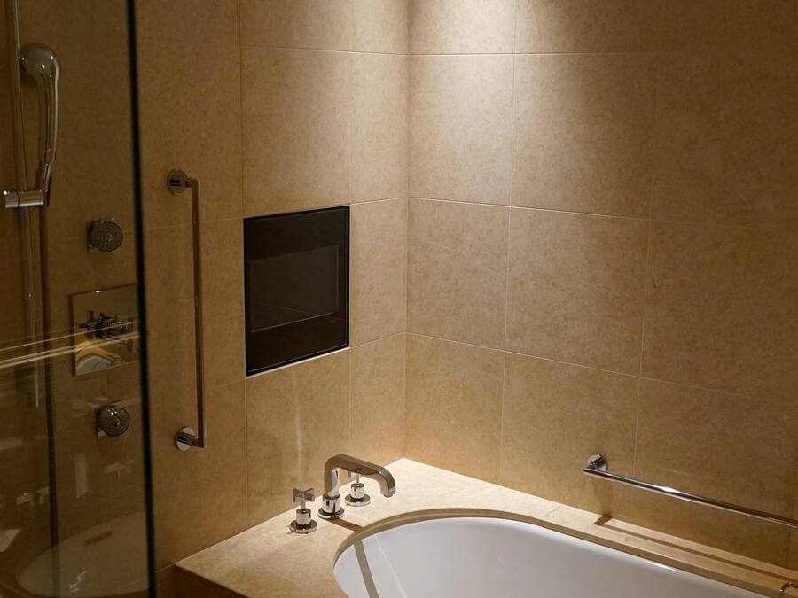 A modern bathroom with a glass-enclosed shower, a large bathtub, and a wall-mounted TV.