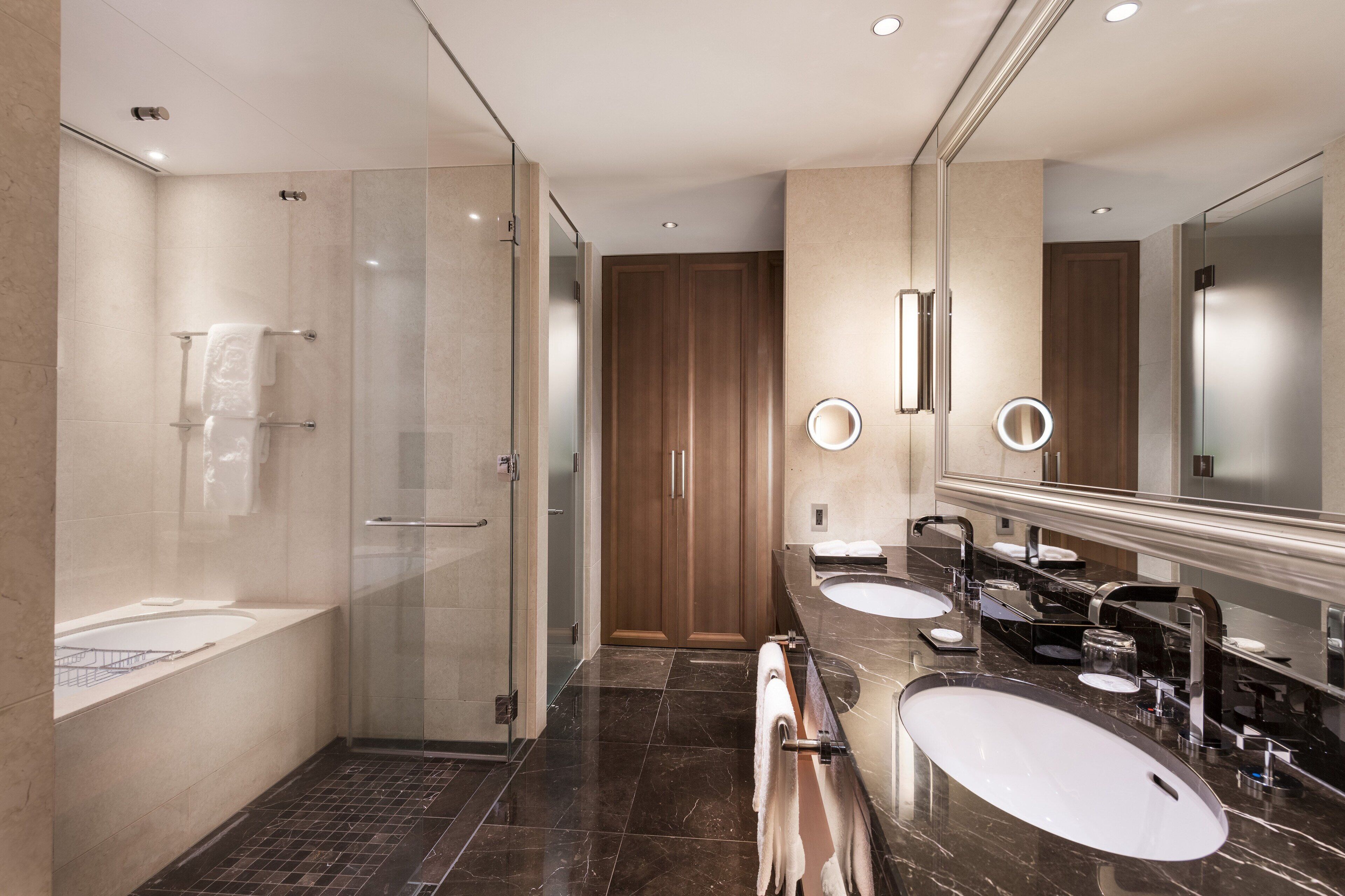 A modern bathroom with a glass-enclosed shower, a vanity with two sinks, and a large mirror.
