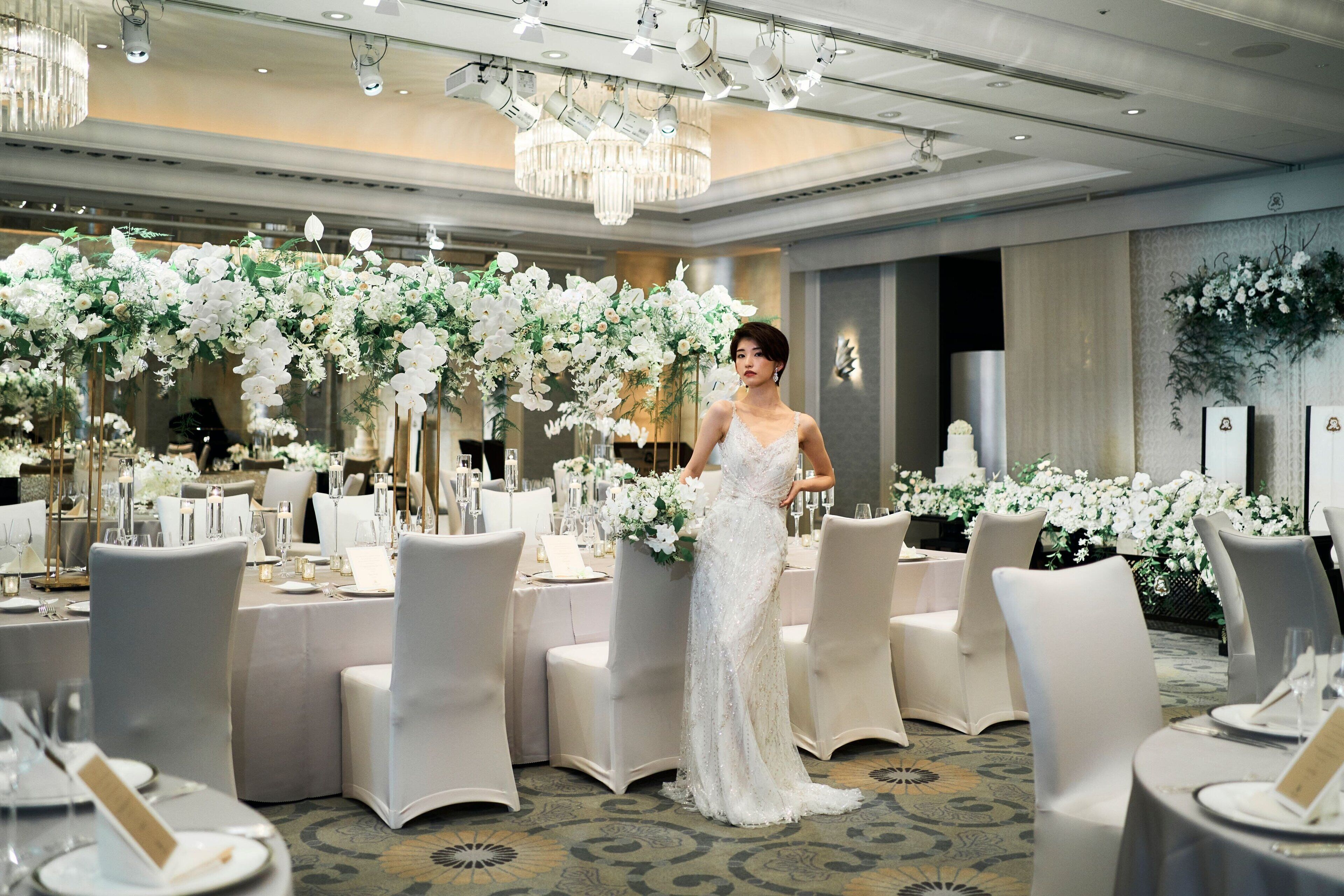 Een feestzaal met ronde tafels, witte stoelen en bloemdecoraties.