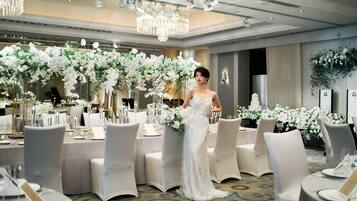 Een feestzaal met ronde tafels, witte stoelen en bloemdecoraties.