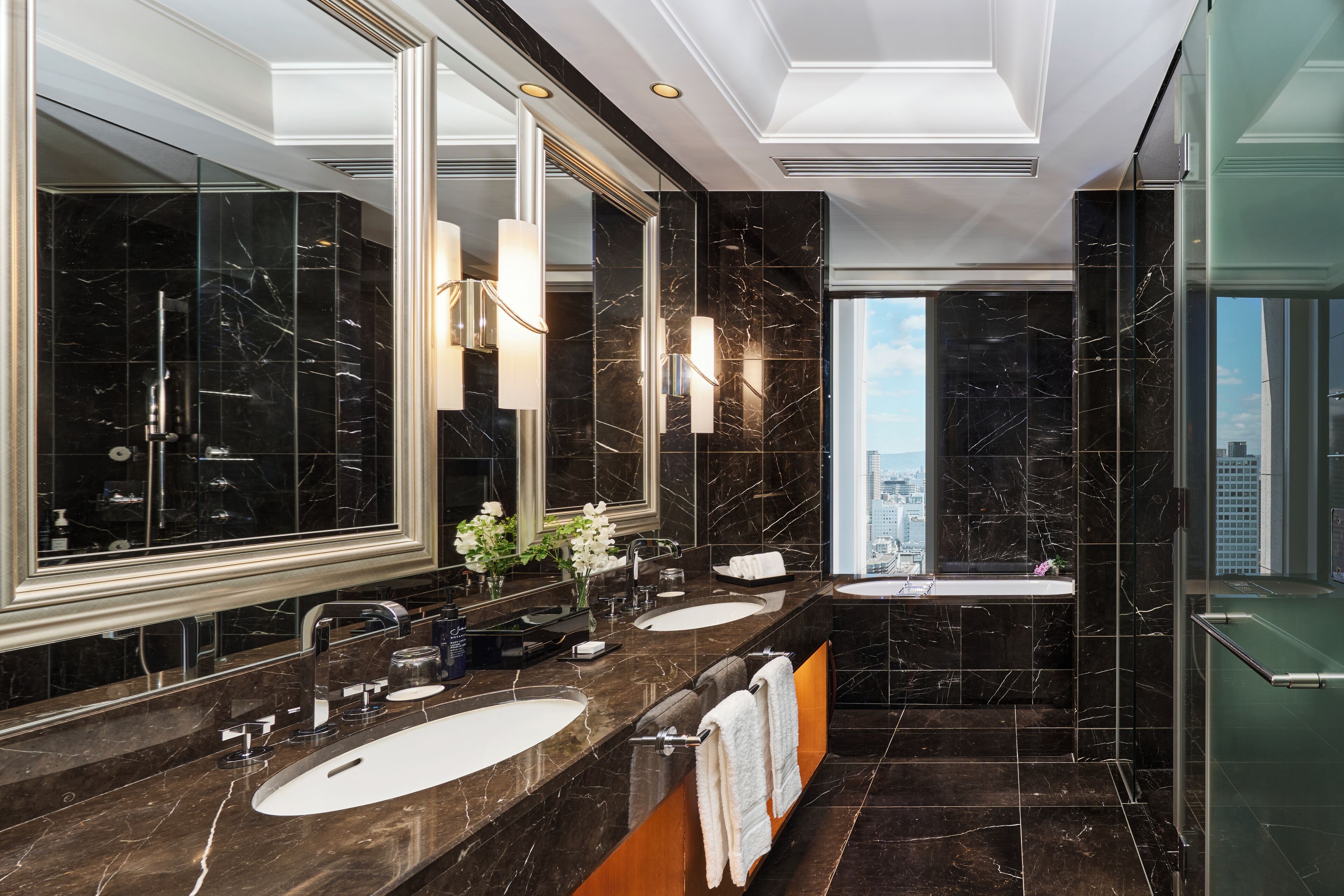 A modern bathroom with two sinks, a large mirror, and a view of the city.