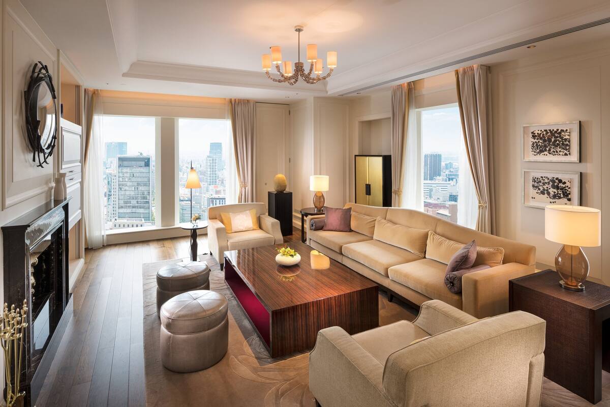 Un salón espacioso con un gran ventanal, chimenea, candelabro y vistas a la ciudad.