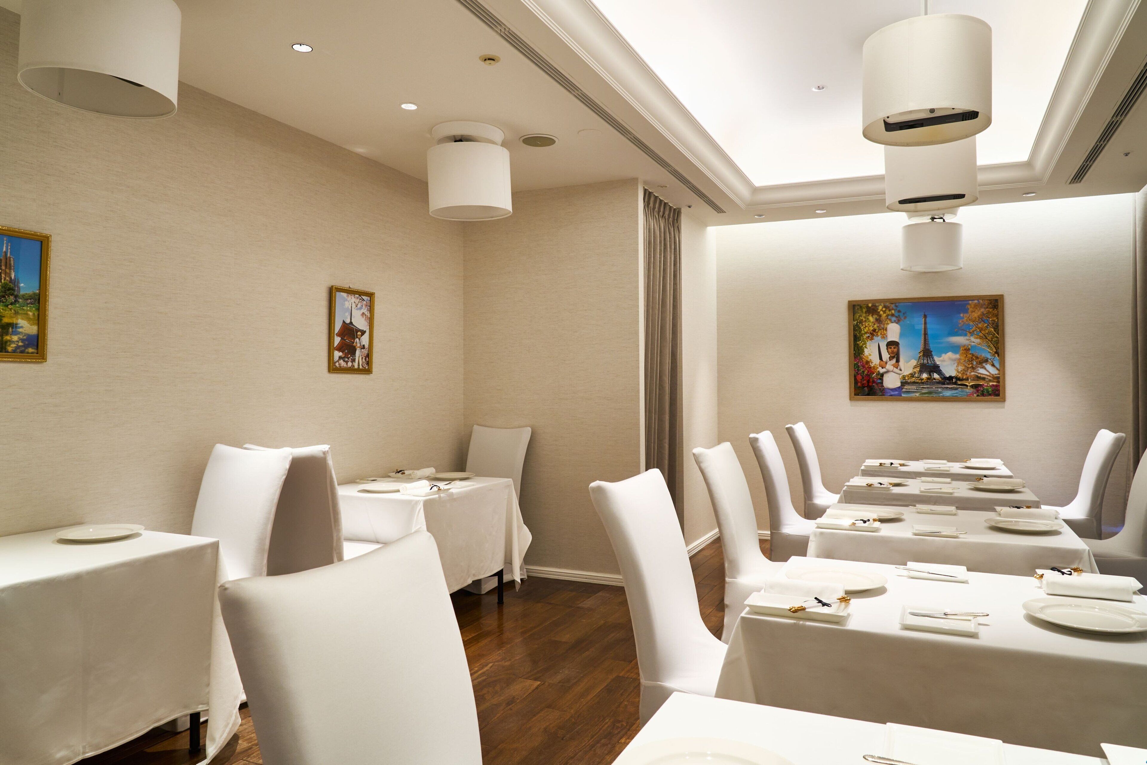 Un comedor con mesas dispuestas para una comida, sillas blancas y cuadros en las paredes.