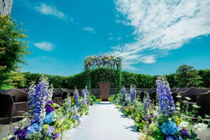An outdoor wedding aisle with floral decorations and wicker chairs on either side.