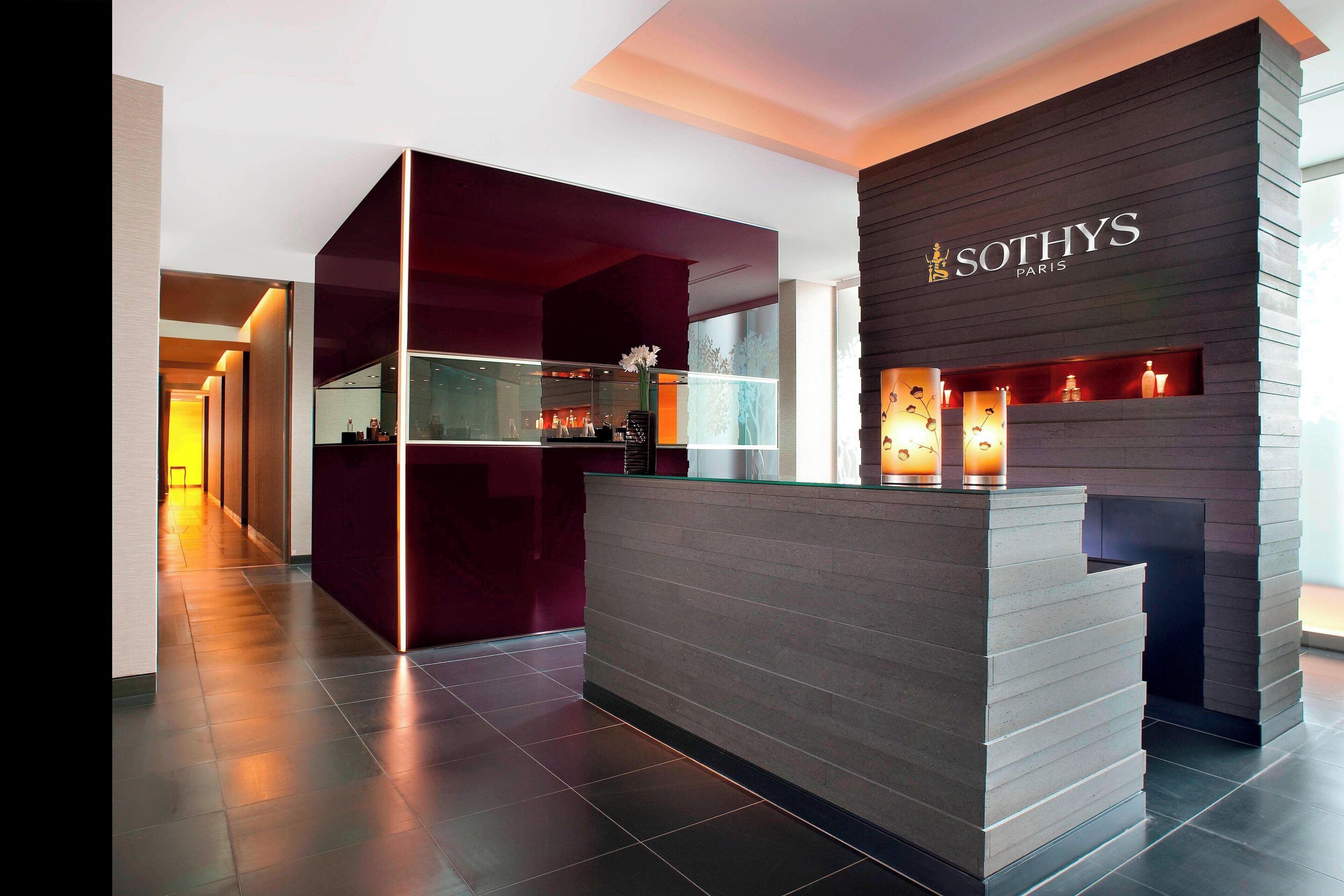 A modern reception area with a reception desk, a dark wooden wall with the name 'Sothys Paris', and a glass partition.