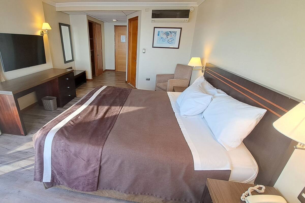 A hotel room with a large bed, bedside tables, a desk, a chair, and a TV.