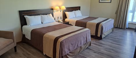 A hotel room with two beds, each with a headboard, bedside tables, lamps, and a framed picture on the wall.