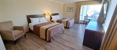A hotel room with two beds, a desk, a chair, and a large window with curtains.