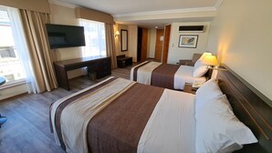 Habitación de hotel con dos camas, un escritorio, un televisor y una ventana con cortinas.