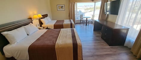 A hotel room with two beds, a desk, a TV, and a balcony with a view.